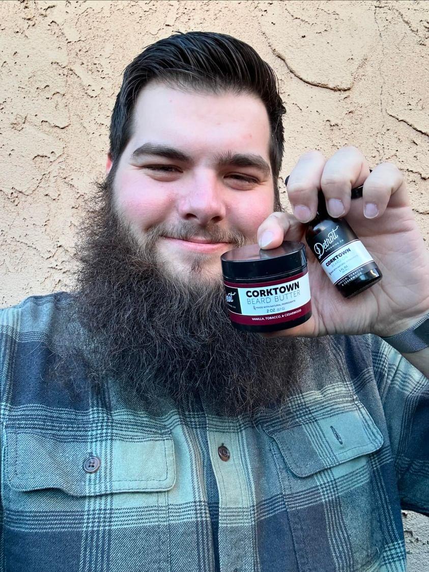 Man with a beard holding beard care products, smiling.