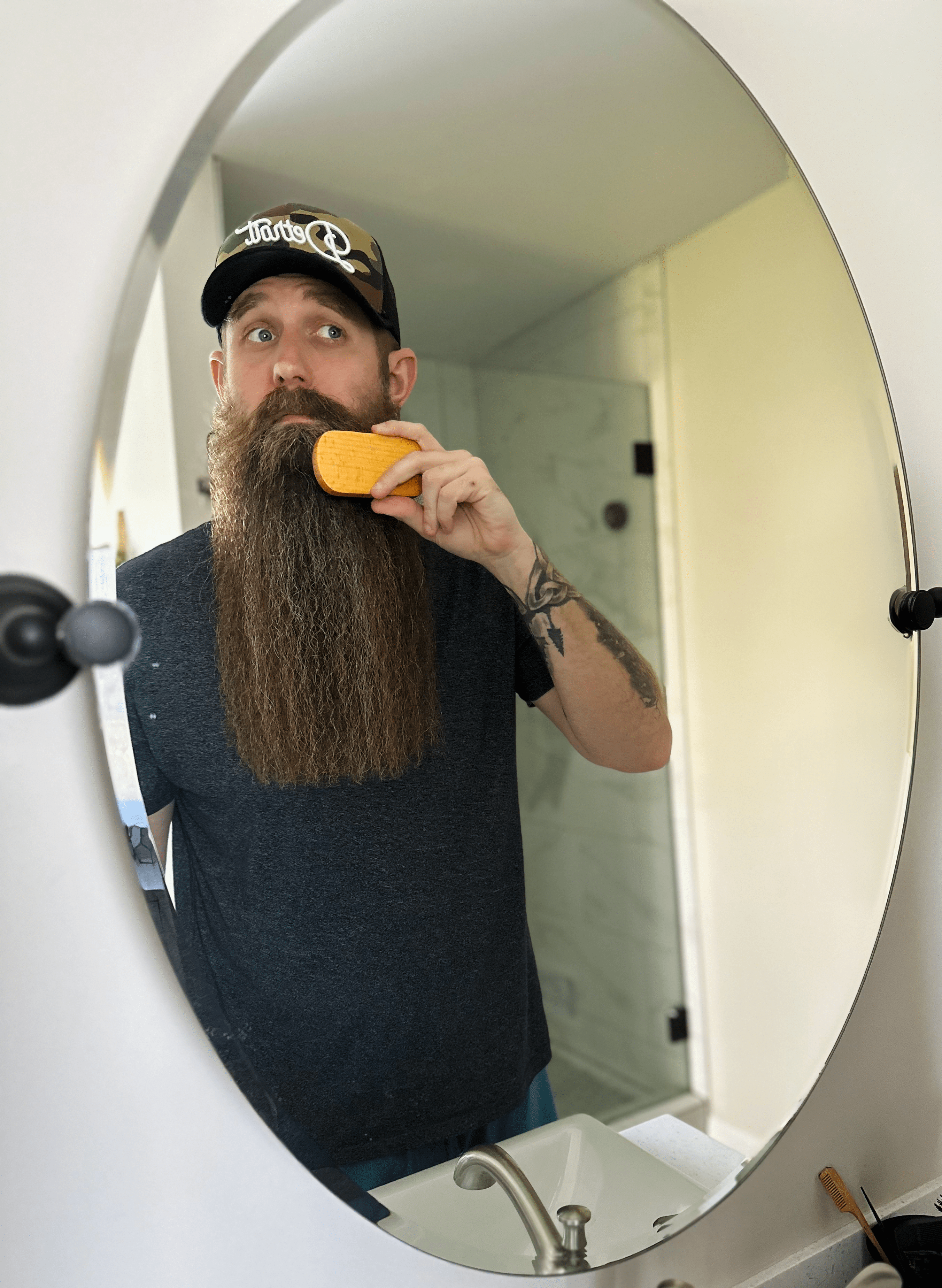 Man with a long beard combing it in front of a mirror.