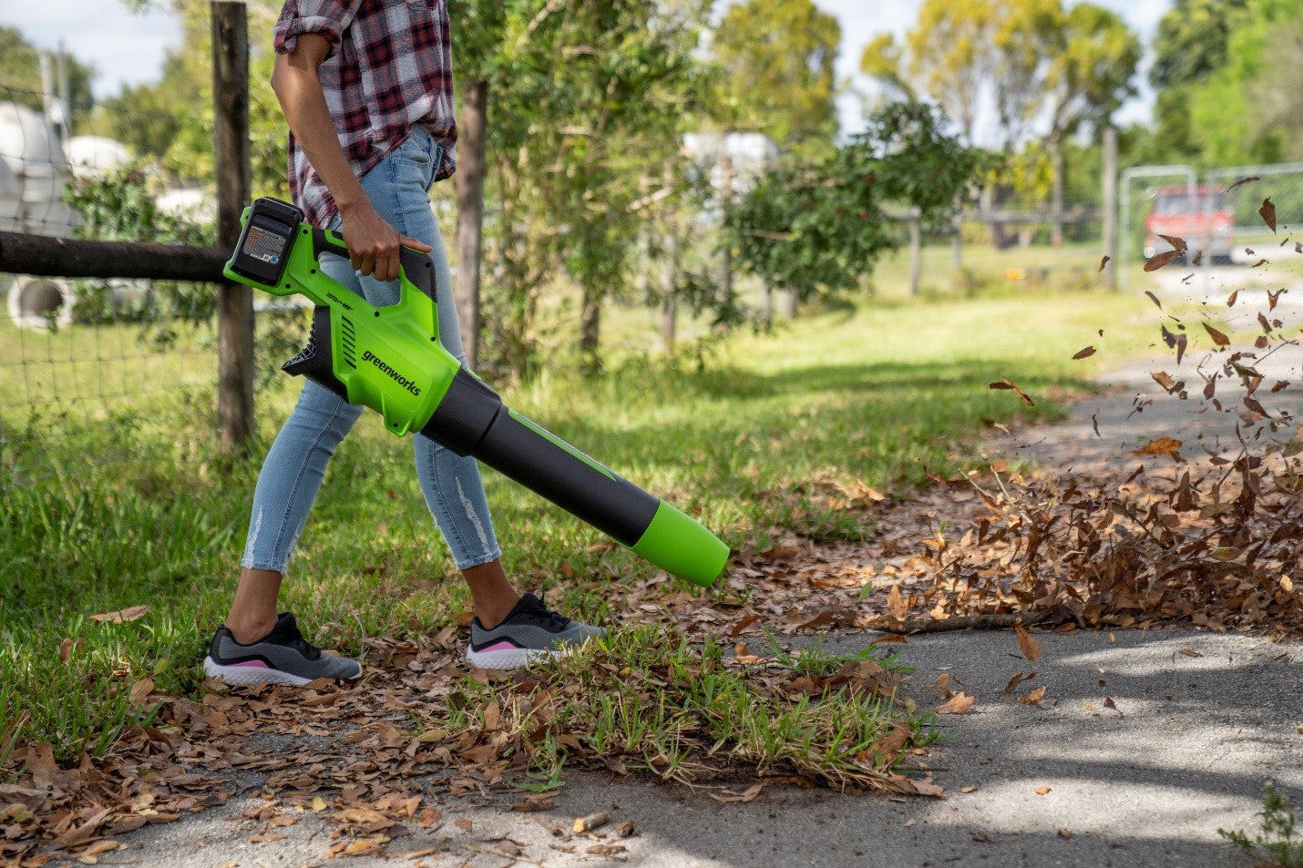 woman using an electric leaf blower to clear path of leaves