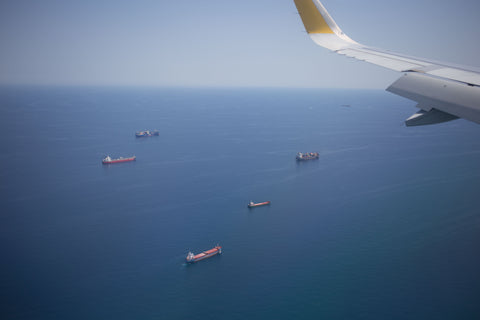 Cargo airplane wing view as container ships are anchored off the coast