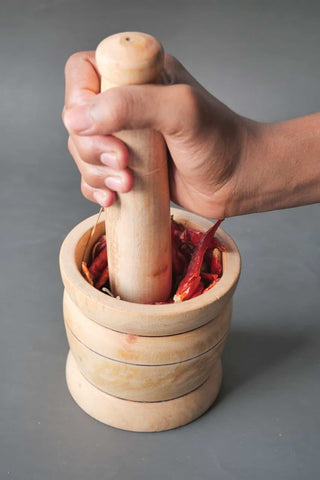 Processing chili flakes in wooden pestle with hands grinding it on a table