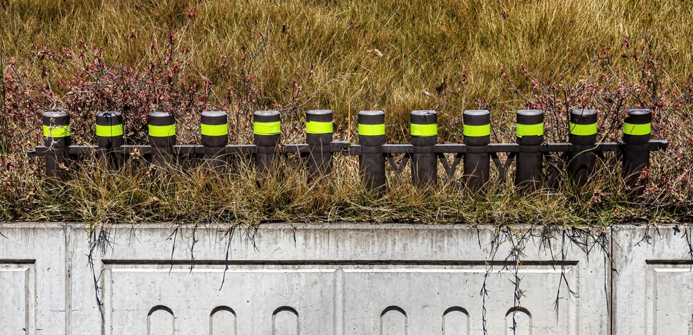 Bright green reflective tapes securely adhered to a sturdy steel fence lining the roadside