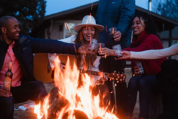 Group of people toasting glasses around a fire.