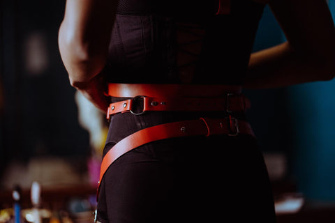 mulher com roupa escura, usando chicote vermelho na cintura