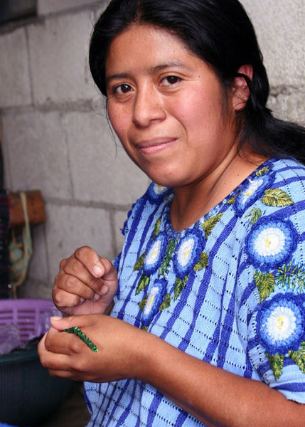 artisan smiling at camera while weaving with beads