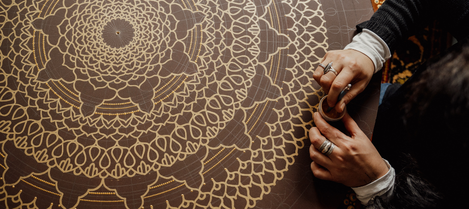 A woman painting a table with a gold mandala