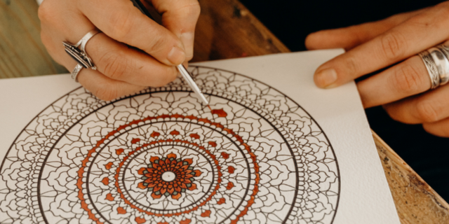 A person coloring a mandala book with a brush and red paint
