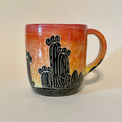 Mug with a cactus silhouette in front of an orange to red sunset sky.