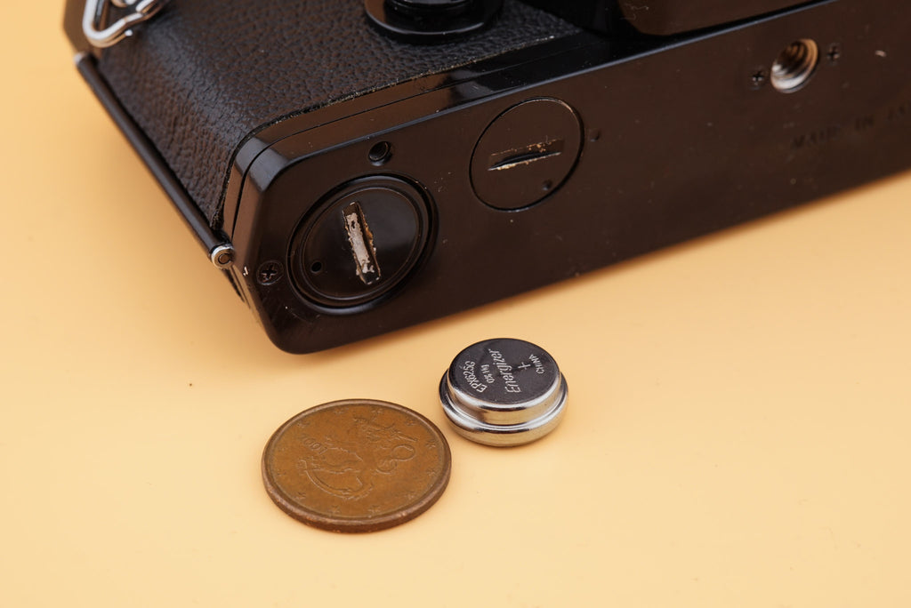 olympus om-1 camera on a table with PX625 battery and a coin