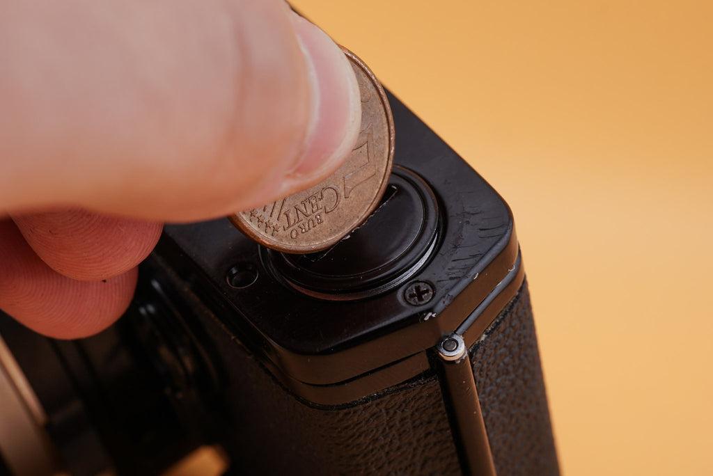 screwing the battery cover of an olympus om-1 camera with a coin