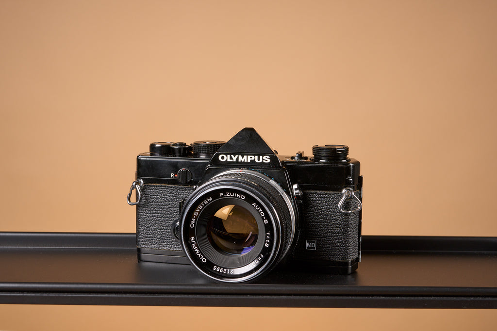 black Olympus OM-1 film camera on a light brown background