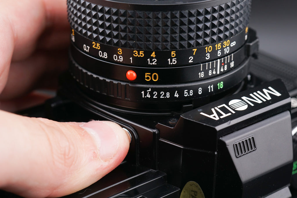 a finger pressing the Minolta X-700 film camera lens release button
