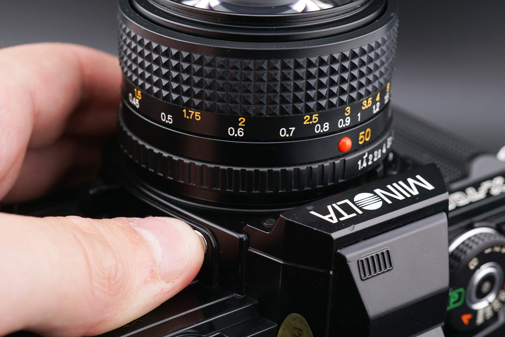 a finger pressing the Minolta X-700 film camera lens release button