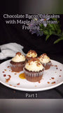 Picture of chocolate Bacon Cupcakes with Maple Buttercream on a white plate with purple flowers and white kitchen towel in background
