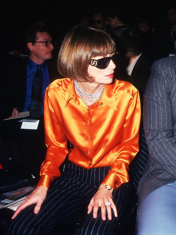 Anna wintour wearing orange satin blouse and black sunglasses