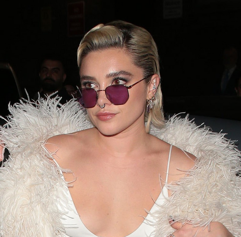 Florence Pugh at the 2024 BAFTAs after party wearing a white gown, white feathered boa, and metal sunglasses with purple lenses.