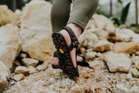 žena v barefoot trekových sandálech jde po skalách