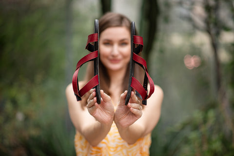 Žena drží v rukou barefoot sandály Ahinsa shoes a ukazuje jejich tenké podrážky