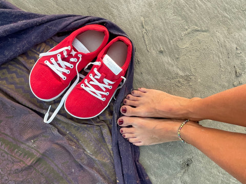 bosé nohy na pláži, vedle nich konopné barefoot tenisky Ahinsa shoes