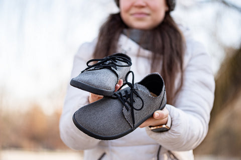žena drží v rukou barefoot boty Ahinsa shoes s širokou špičkou