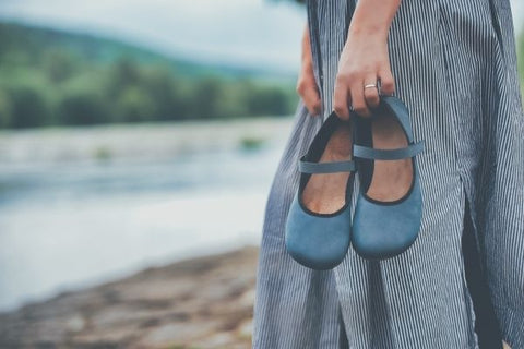 žena kráčí podél řeky a v ruce drží barefoot balerínky Ahinsa shoes