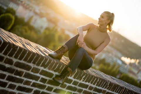 žena v barefoot botách sedí na zídce v západu slunce a usmívá se