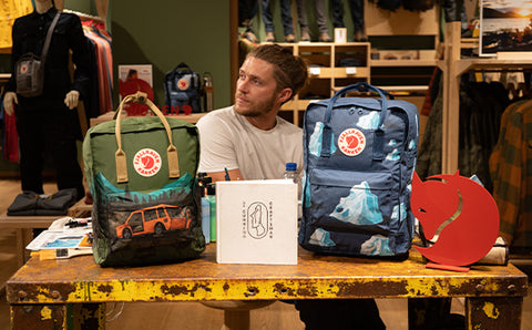 Craftsman at a workshop table with two special edition Fjällräven Kånken backpacks and outdoor gear, in a Fjällräven store