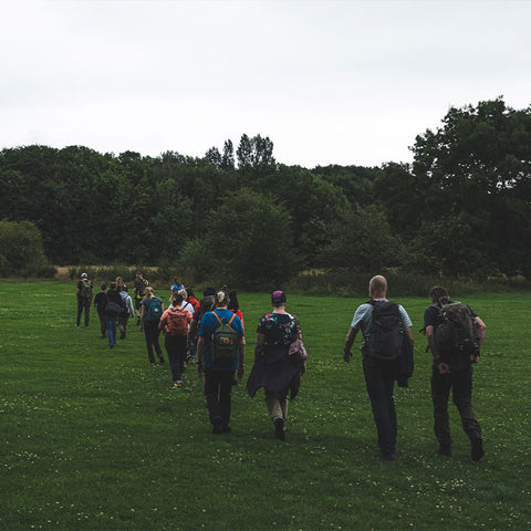 Participants of the Fjällräven Walk in Manchester trek across a lush green field, with some sporting colourful Fjällräven backpacks.