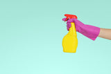 Pink gloved hand holds a yellow bottle of cleaner against a blue background