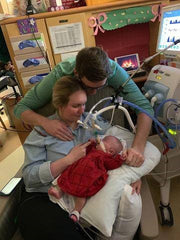 mother holding baby with father leaning over at hospital
