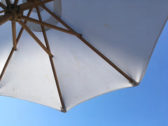 looking up at white shade umbrella outdoors with a blue sky