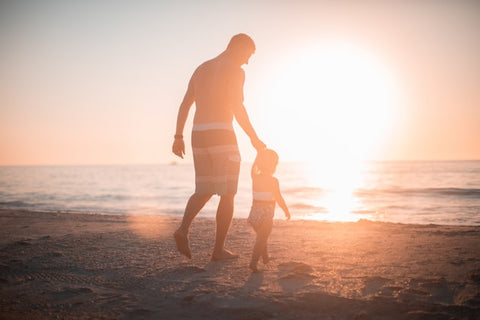 Silhouette of a man and child walking on a beach with the sun in the background