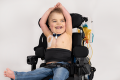 boy seated in wheelchair with arms raised wearing black stretch waistband