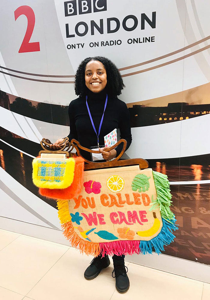 Image of Tihara Smith holding raffia bags in front of a BBC Radio London sign