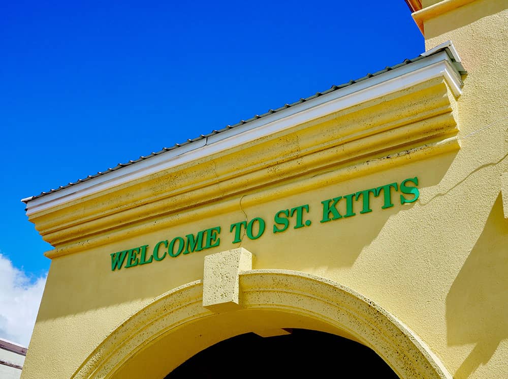 Image of a pastel yellow building with 'Welcome to St. Kitts' written on the top in green block letters.