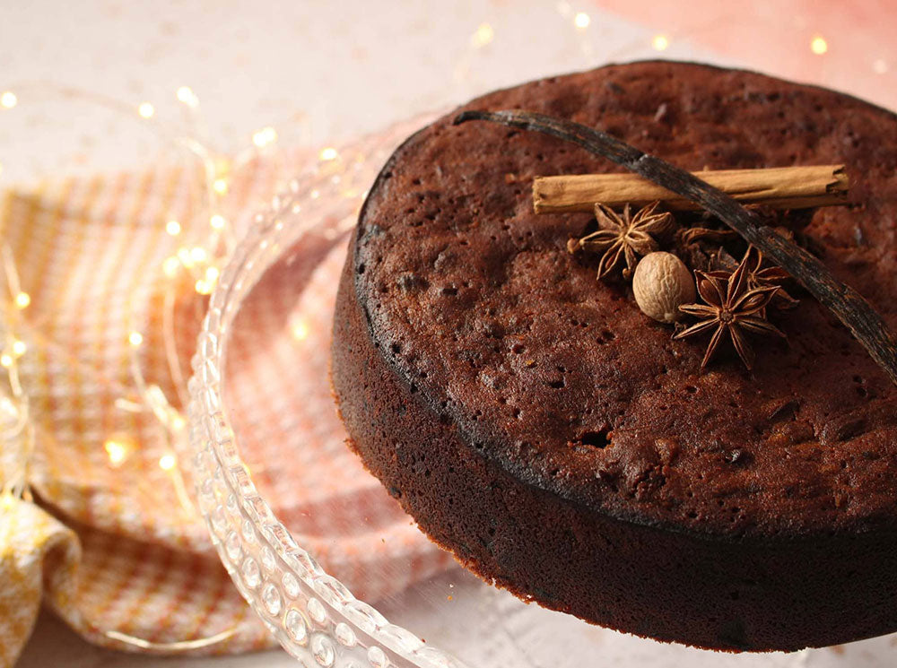 Image of a rum cake on a clear cake stand with spices on top of the cake.