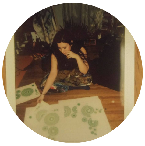 artist CA Reid sits on the floor wearing colorful paint splattered coveralls. She inspects freshly printed silkscreen prints of green mandalas encoded with a secret message.