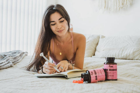 A girl is writing in her diary on her bed with Bra Bearies gummies