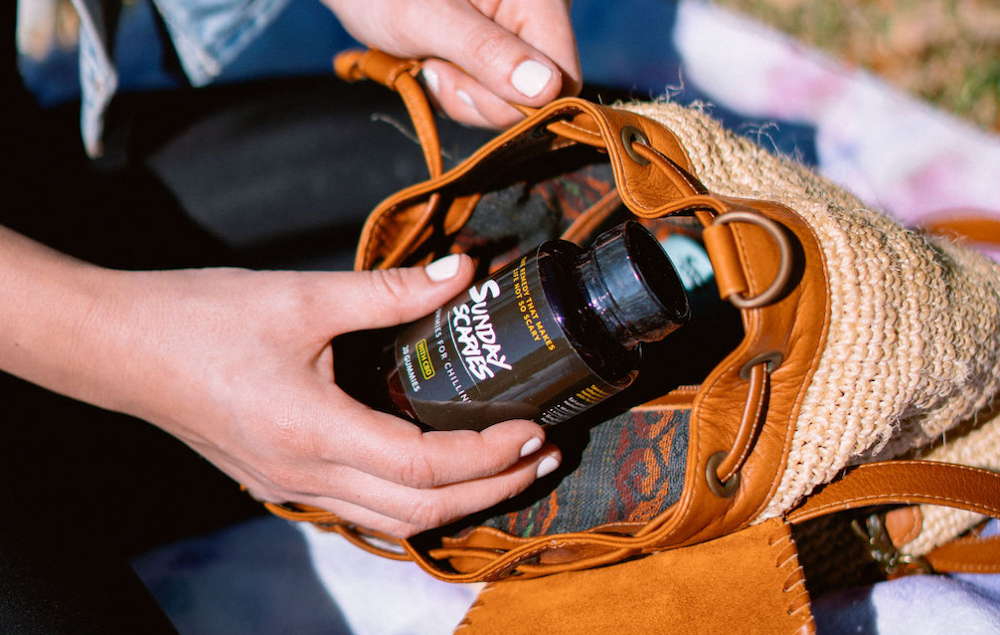 A woman takes a bottle of Sunday Scaries CBD gummies out of her backpack