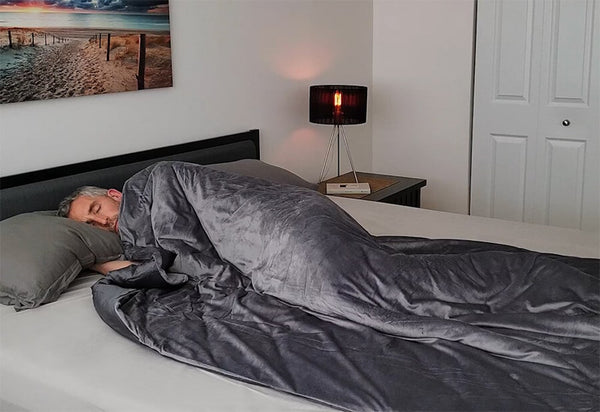 A man curls up in his Luxome weighted blanket on his bed