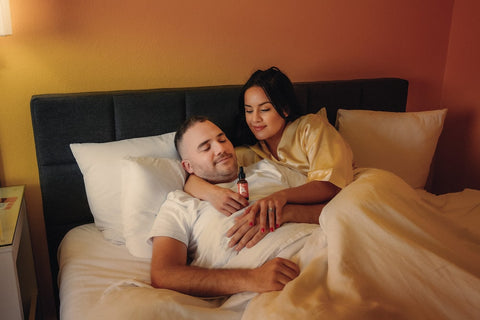 A couple is snugging in bed while the wife wraps her arm around her husbands neck