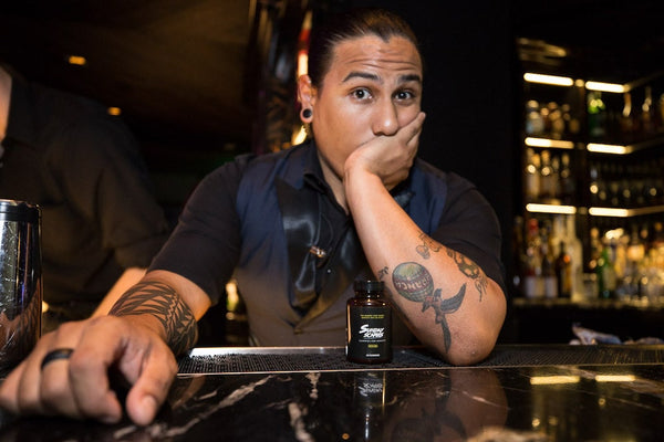 A bartender with tattoos behind the bar looks like he's questioning the patron with a bottle of Sunday Scaries in front of him