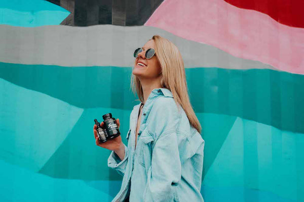 A blonde millennial holds the Sunday Scaries Sidepiece bundle in her hands in front of a colorful wall