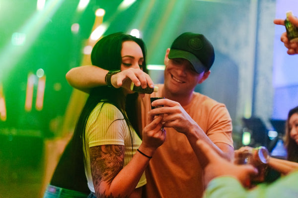 A guy embraces his girlfriend at a nightclub as he pours a shot for her
