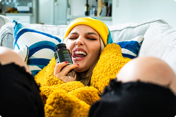 A girl with a yellow beanie snuggles up on her couch hungover with a bottle of Sunday Scaries in her hand