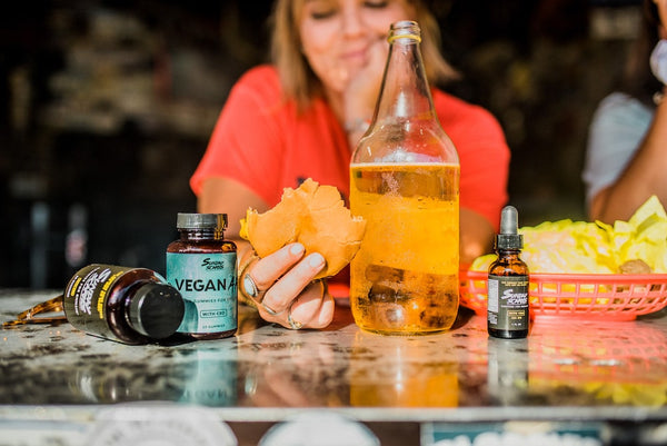 A girl holds a half eaten cheeseburger while drinking a bottle of beer surrounded by Sunday Scaries products