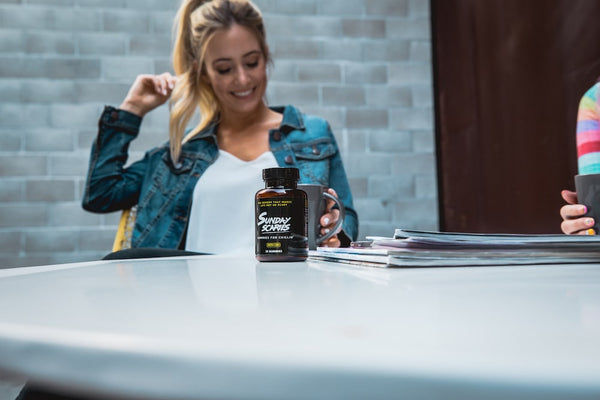 A girl sits at a table with a bottle of Sunday Scaries CBD gummies while relaxing and drinking coffee