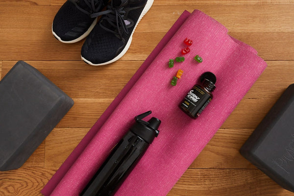 A water bottle and a bottle of Sunday Scaries are placed on a yoga mat surrounded by shoes and yoga blocks