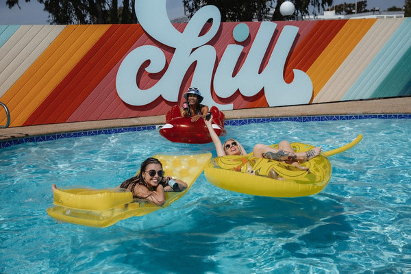 Three girls enjoy the pool during the summer with a "Chill" sign on the wall in the background