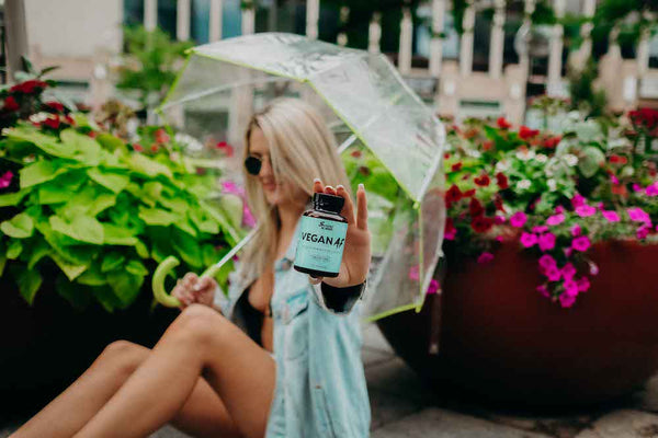 A woman holds up a bottle of Sunday Scaries Vegan AF gummies in a garden while holding an umbrella